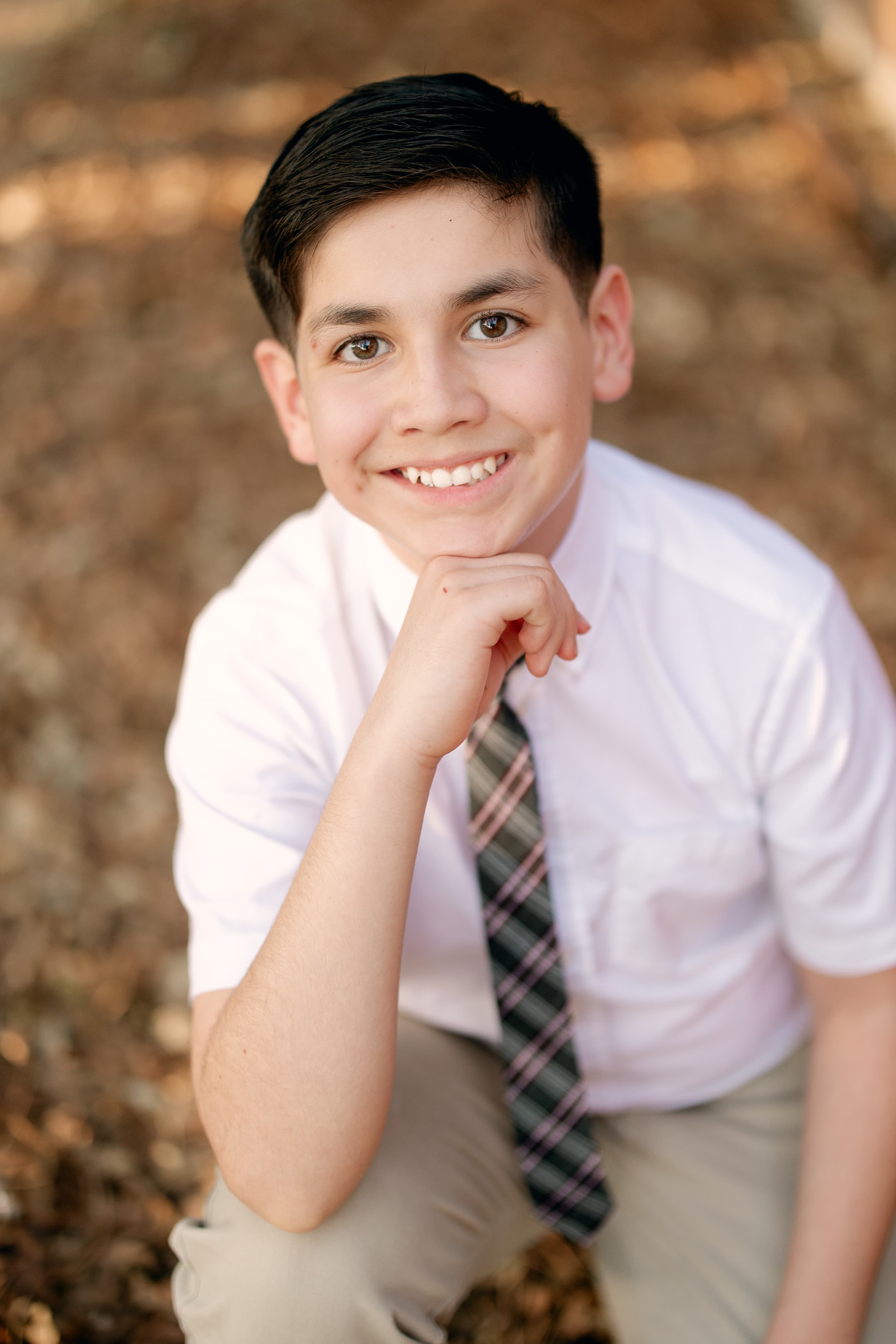 Young boy in white shirt and plaid tie smiling warmly